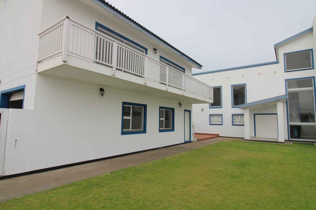 A view of the rear exterior of the house, featuring a white facade with blue trim, a balcony, and a well-maintained lawn area.