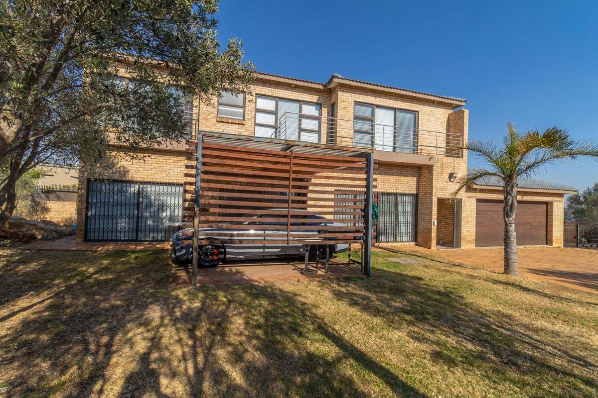 Rear view of a double-story face brick house featuring a balcony, timber pergola, paved driveway, and double garage.