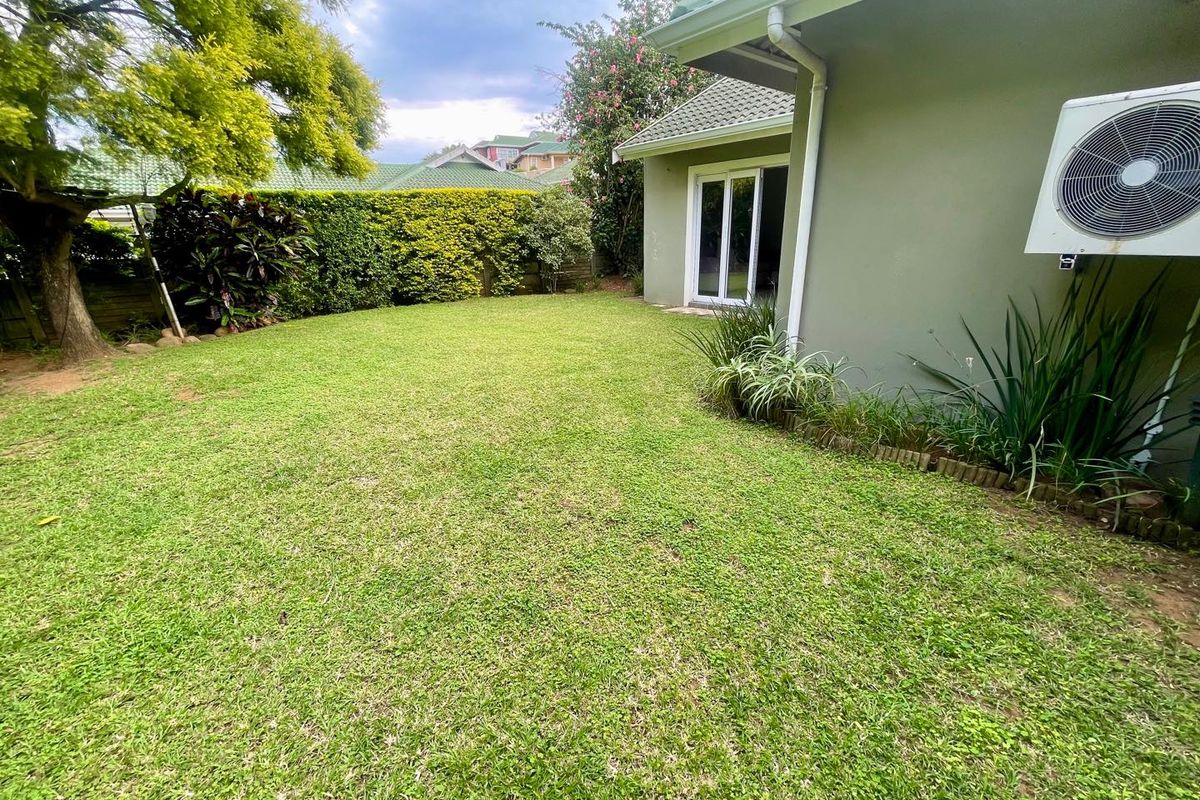 A well-maintained rear garden featuring a lush green lawn, established perimeter hedging, and direct access to the home via sliding glass doors.