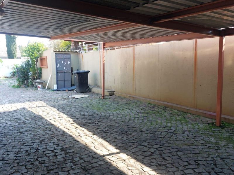 A covered outdoor carport area featuring cobblestone paving and a perimeter boundary wall, providing sheltered parking space.
