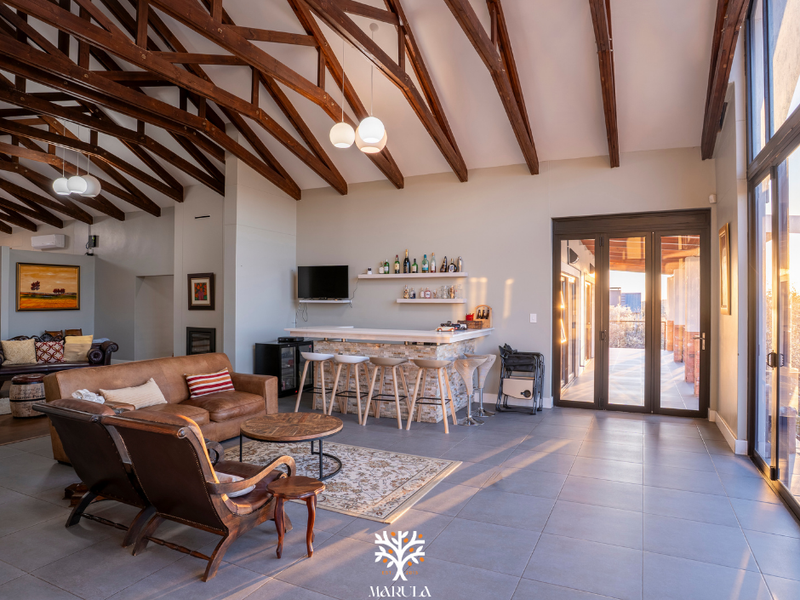 Spacious open-plan living area featuring high exposed timber trusses, a built-in bar with stone detailing, and large sliding doors leading to the patio.