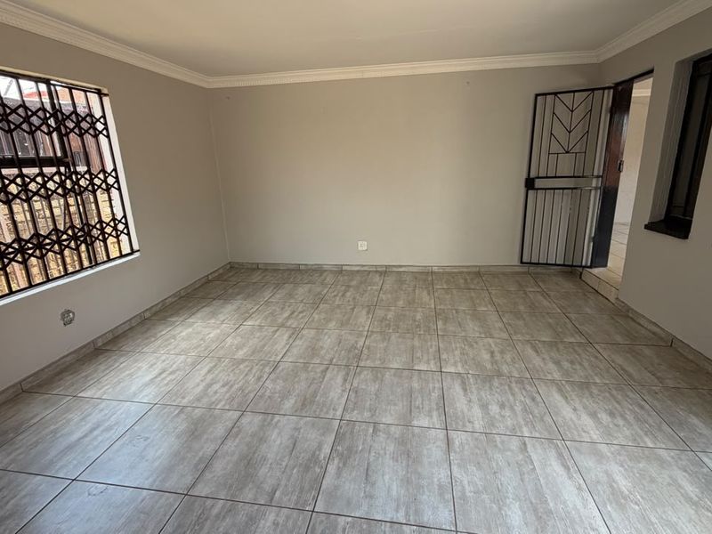 A spacious, empty living room featuring neutral wall paint, modern wood-look ceramic floor tiles, and secure window and door fixtures.