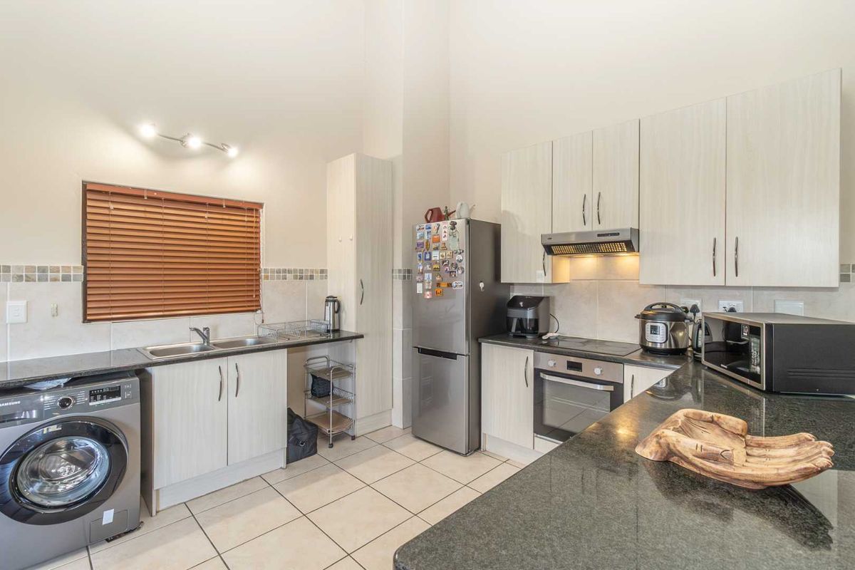 A functional kitchen featuring granite countertops, built-in cabinetry, an integrated oven with extractor fan, and tiled flooring with a dedicated laundry appliance space.