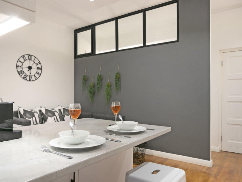 Modern kitchen area featuring a stone-topped island, sleek grey accent wall with transom window, and classic panelled door.