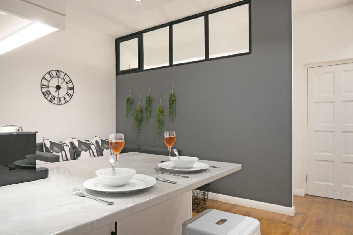 Modern kitchen area featuring a stone-topped island, sleek grey accent wall with transom window, and classic panelled door.