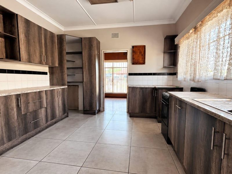 A functional kitchen featuring dark wood-look cabinetry, stone-effect countertops, tiled flooring, and a built-in pantry, offering a clean and practical workspace.