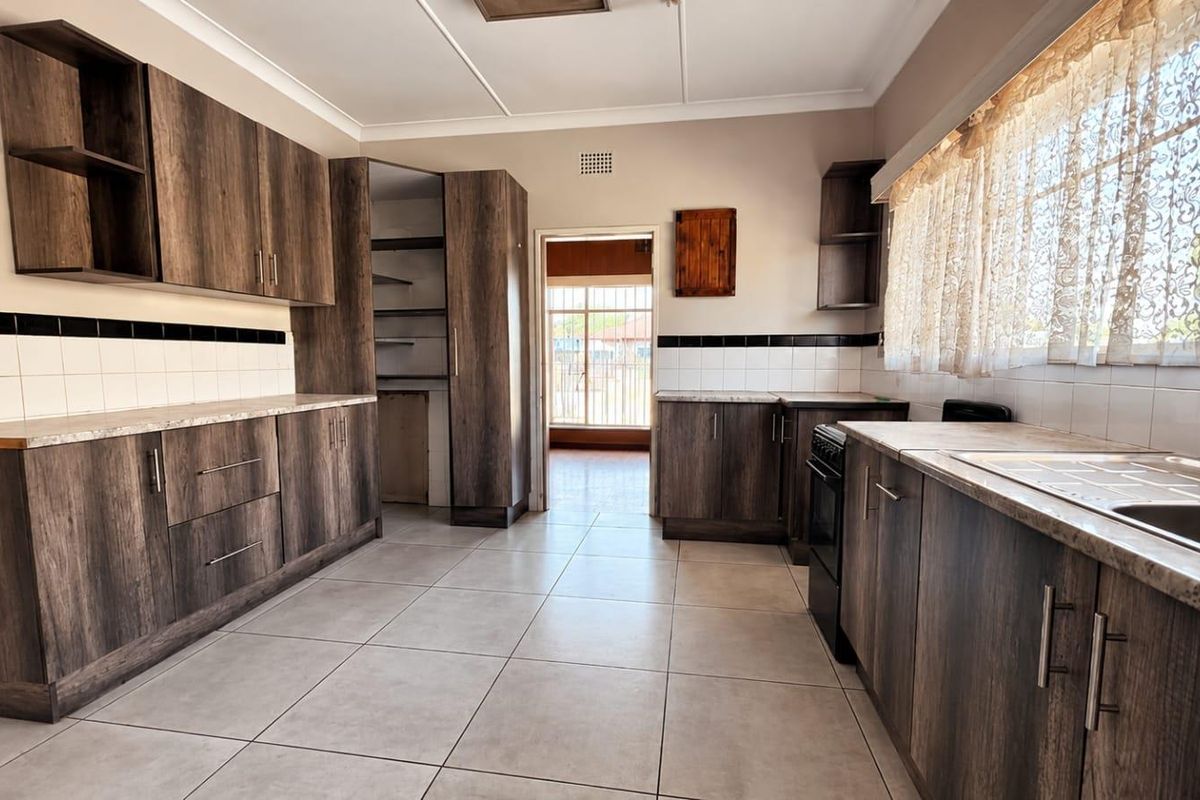 A functional kitchen featuring dark wood-look cabinetry, stone-effect countertops, tiled flooring, and a built-in pantry, offering a clean and practical workspace.