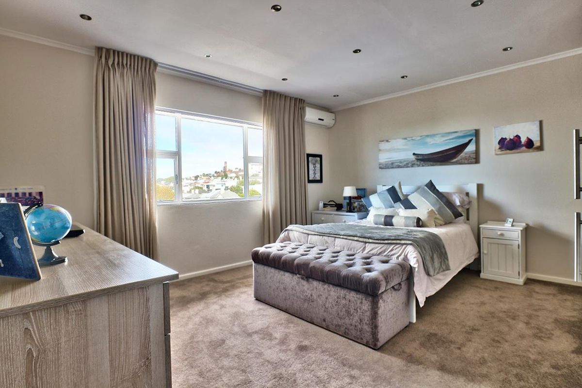 A well-maintained bedroom featuring neutral carpeting, recessed downlighting, and a wall-mounted air conditioning unit with natural light from the window.