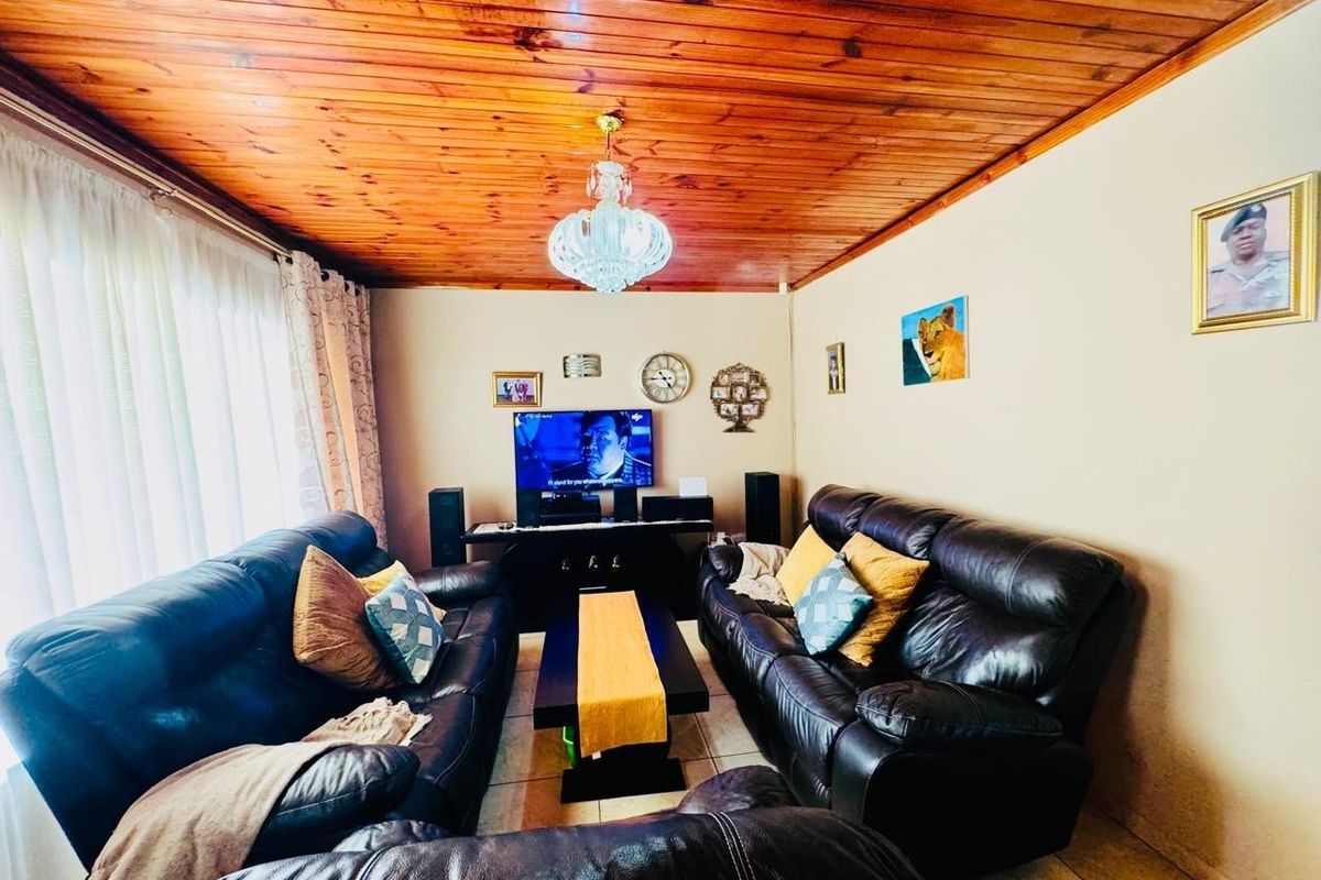 A cozy living room featuring a warm timber-clad ceiling, tiled flooring, and a central crystal chandelier, providing a comfortable and inviting atmosphere.