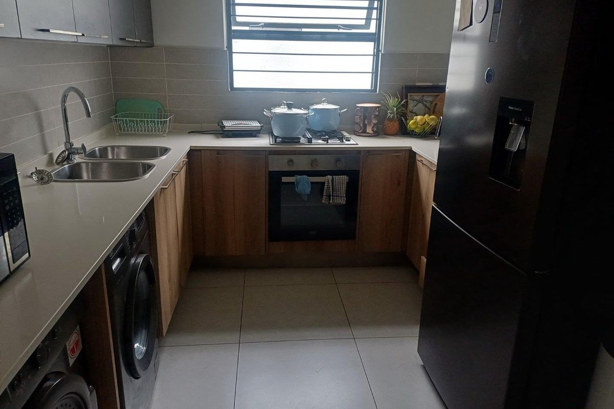 A functional kitchen featuring light wood cabinetry, stone countertops, a built-in oven, gas hob, and integrated laundry appliances.