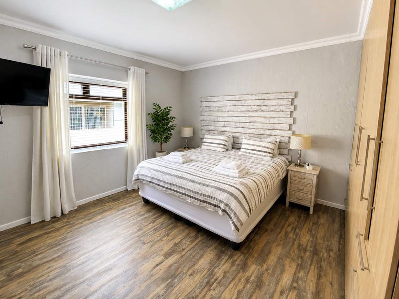 A well-maintained bedroom featuring wood-look laminate flooring, neutral wall finishes, and a large built-in wardrobe.