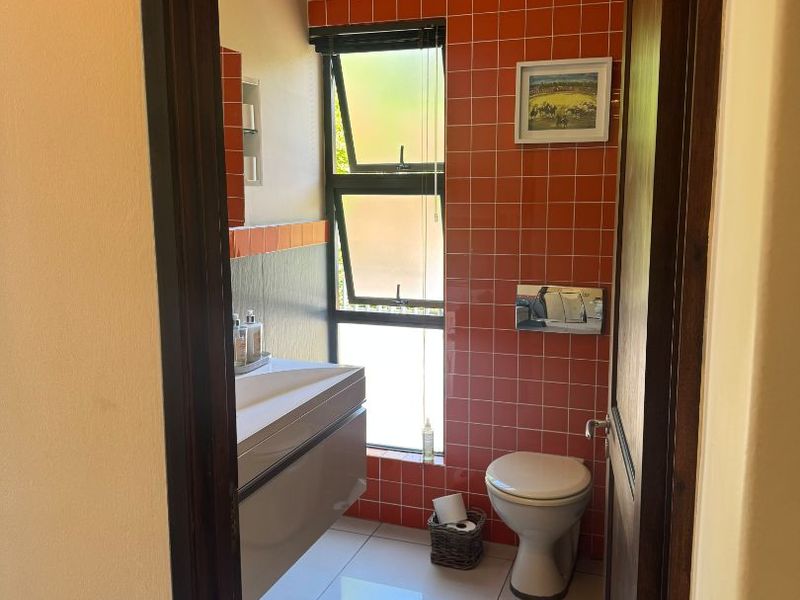 A compact bathroom featuring vibrant orange wall tiles, a modern wall-mounted vanity, and a top-flush toilet with a top-hung window for natural light.