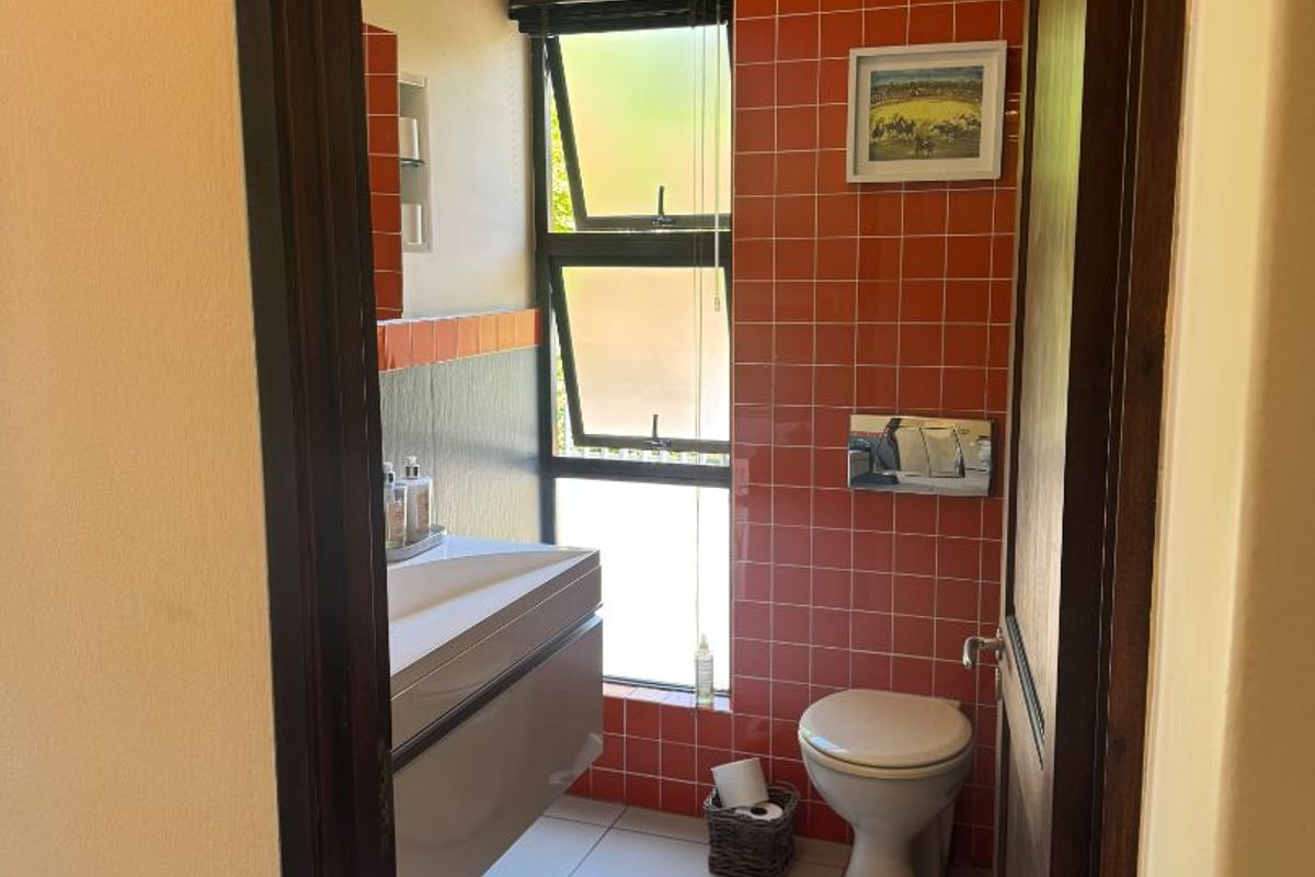 A compact bathroom featuring vibrant orange wall tiles, a modern wall-mounted vanity, and a top-flush toilet with a top-hung window for natural light.