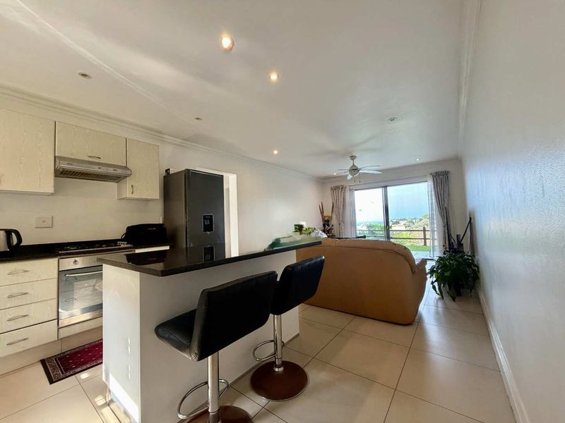 Open-plan living area featuring a functional kitchen with granite countertops, built-in appliances, and a breakfast bar, flowing into a bright lounge with balcony access.