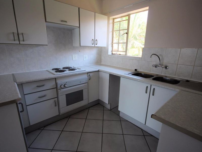 A functional kitchen featuring white cabinetry, laminate countertops, an electric hob, built-in oven, and a double bowl sink with tiled splashbacks.