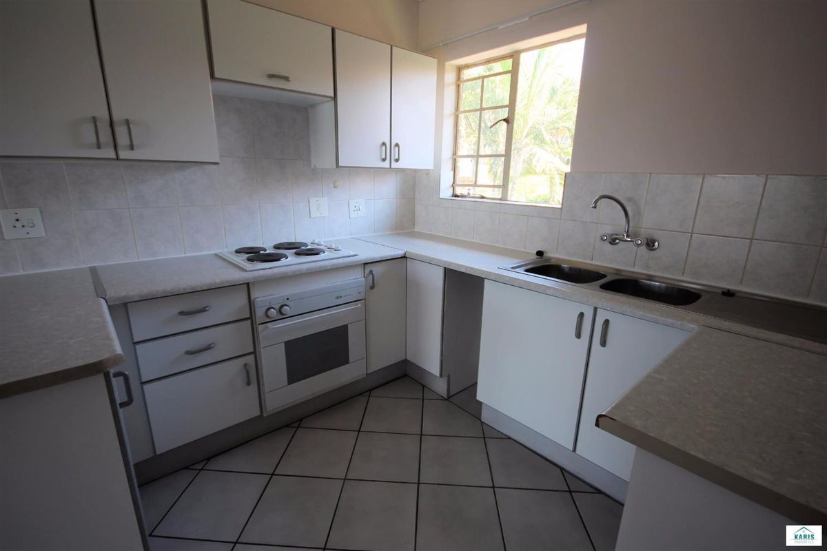 A functional kitchen featuring white cabinetry, laminate countertops, an electric hob, built-in oven, and a double bowl sink with tiled splashbacks.