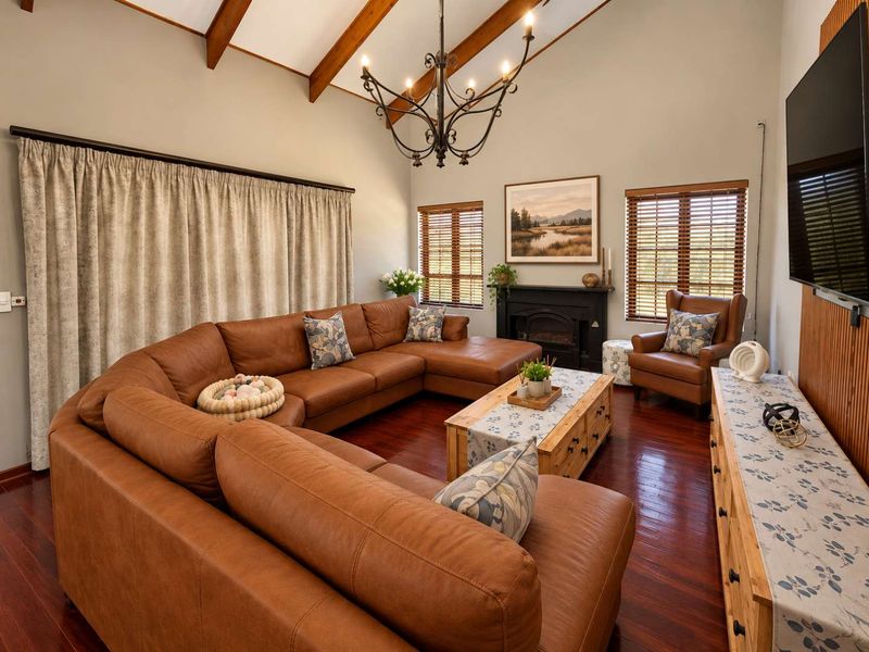 Spacious living room featuring vaulted ceilings with exposed timber beams, rich hardwood flooring, and a cozy fireplace, creating a warm and inviting atmosphere.