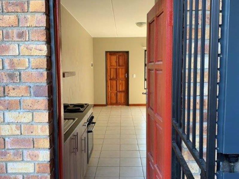 A view through a security gate into an empty kitchen featuring tiled floors, built-in cabinetry, and a fitted oven and hob.