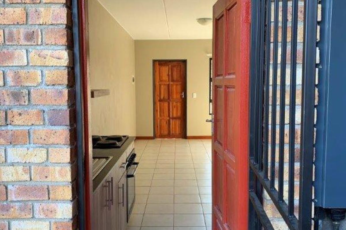 A view through a security gate into an empty kitchen featuring tiled floors, built-in cabinetry, and a fitted oven and hob.