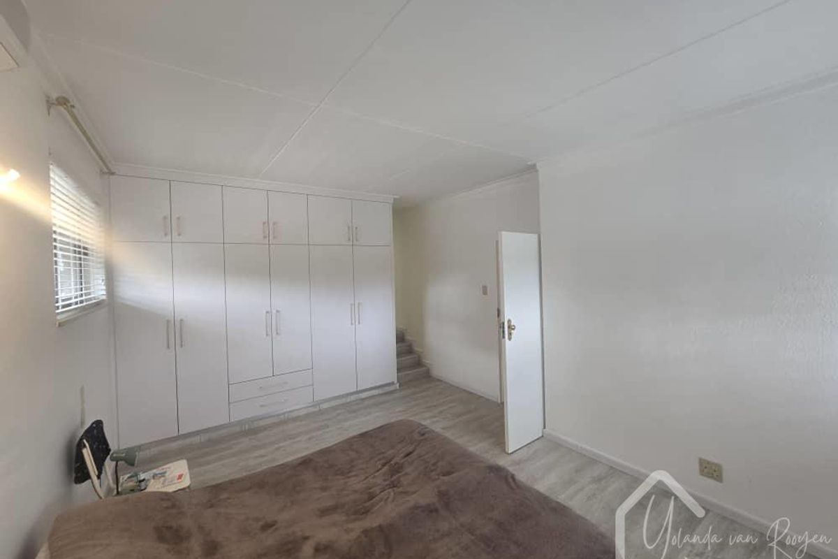 A bedroom featuring built-in floor-to-ceiling white cabinetry, light-toned laminate flooring, and a neutral color palette.