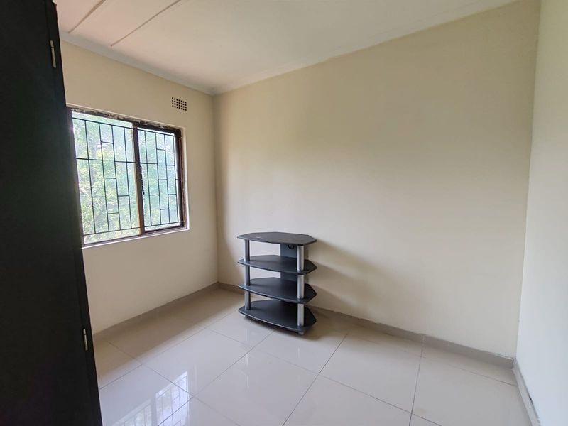 A bright, empty bedroom featuring neutral tiled flooring, a window with security bars, and a built-in cupboard, offering a clean canvas for personalization.
