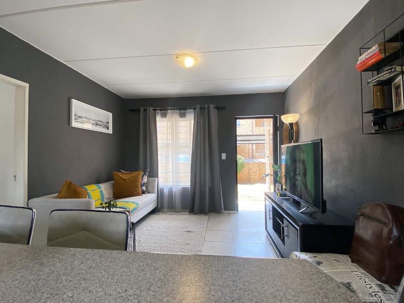An open-plan living area featuring tiled flooring, dark painted walls, and direct access to an outdoor space through a rear door.