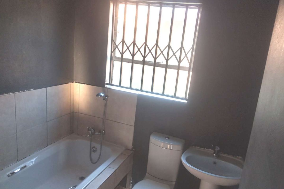 A functional bathroom featuring a bathtub with shower mixer, pedestal basin, and toilet, complemented by a security gate on the window.