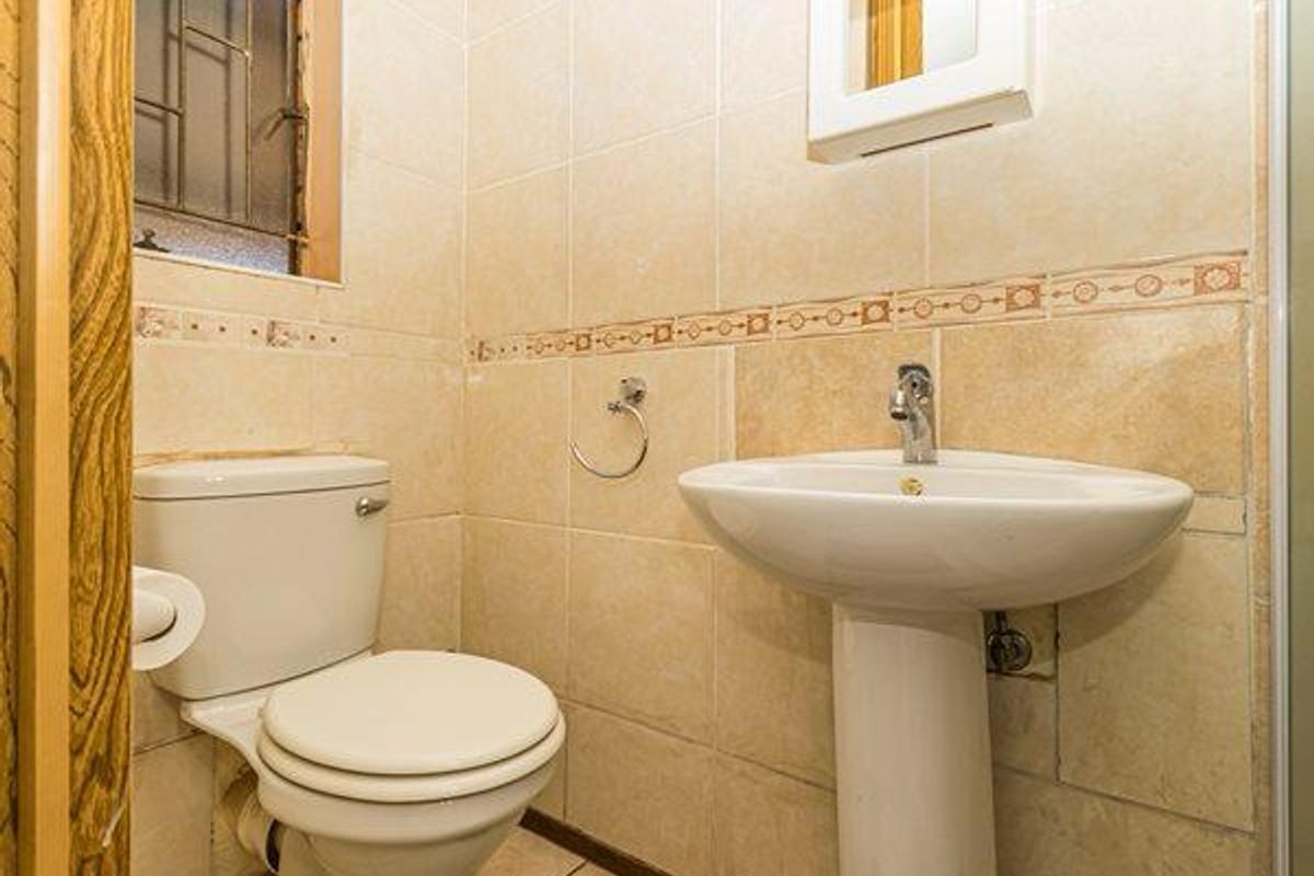 A compact bathroom featuring a pedestal basin, a standard toilet, and floor-to-ceiling ceramic wall tiling with a decorative border.