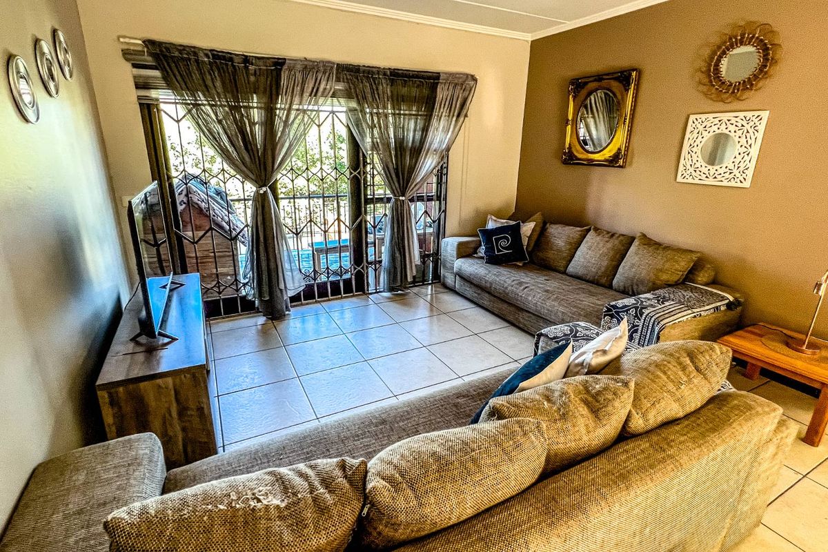 A comfortable living room featuring tiled flooring and a large sliding door with security gate, providing access to an outdoor area.