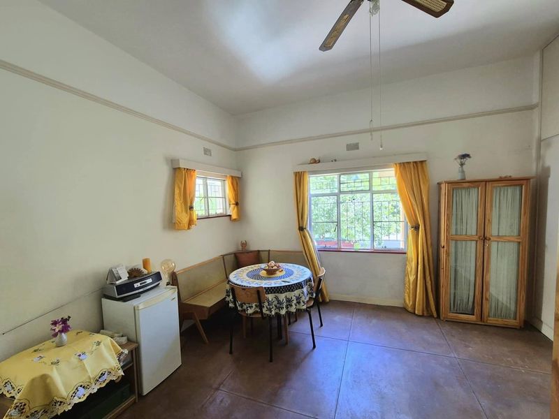 A living area featuring tiled flooring, a ceiling fan, and large windows with security bars, offering a functional and well-lit space.