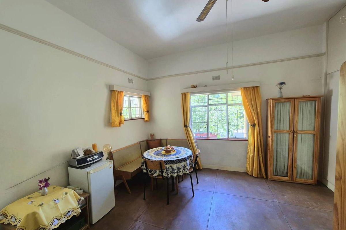 A living area featuring tiled flooring, a ceiling fan, and large windows with security bars, offering a functional and well-lit space.