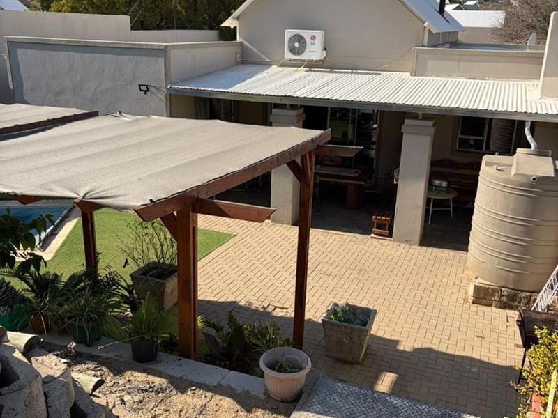 Rear exterior view featuring a paved courtyard, covered patio area, timber pergola, and a water storage tank.