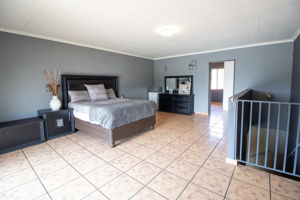 Spacious bedroom featuring ceramic floor tiles, grey painted walls, and a metal staircase railing leading to the lower level.