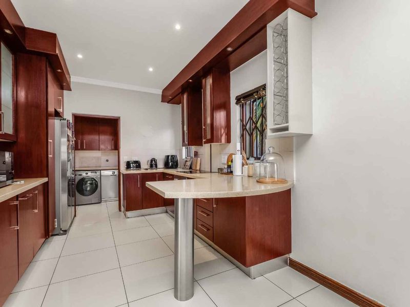 A well-maintained kitchen featuring rich wood cabinetry, stone countertops with a breakfast bar, tiled flooring, and an adjacent laundry area.