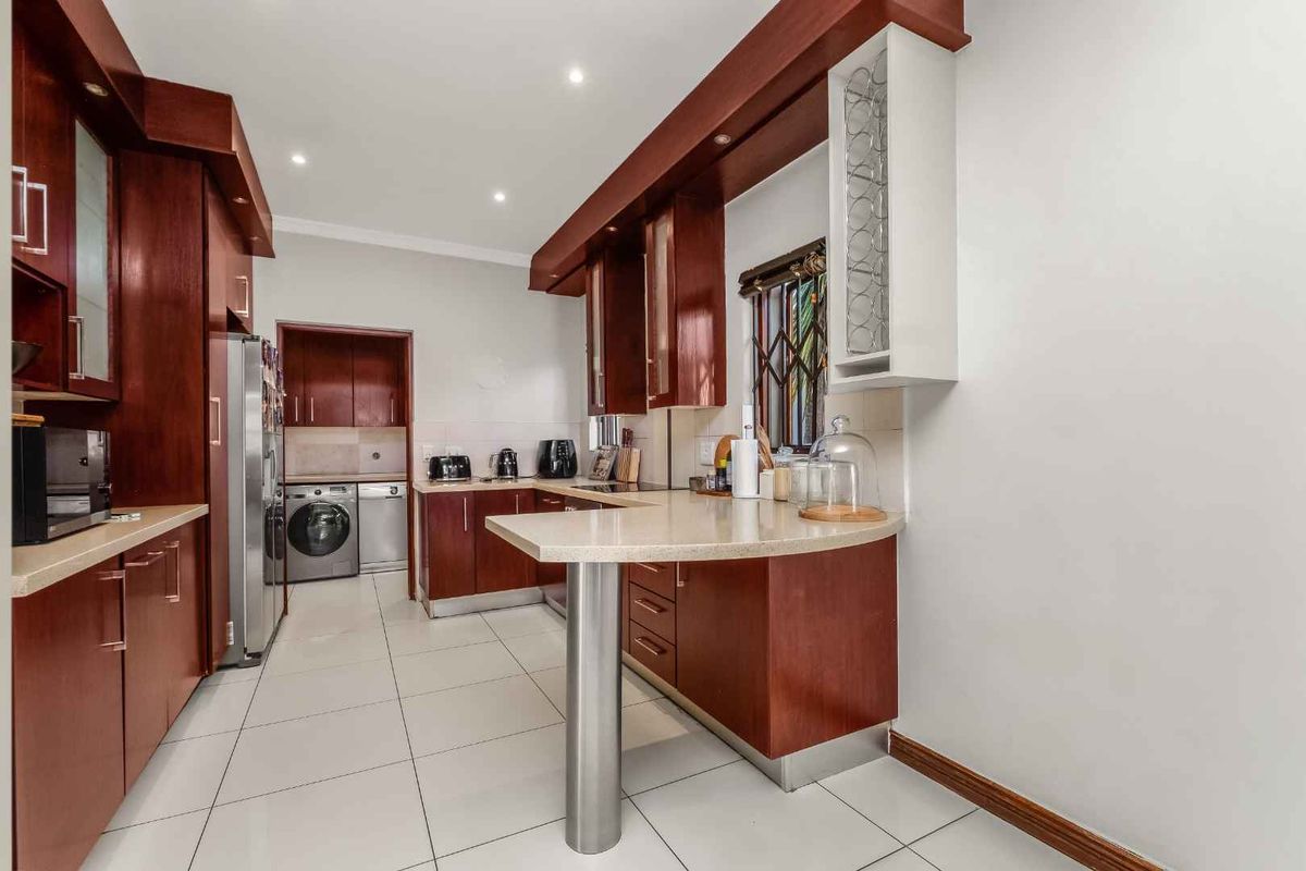 A well-maintained kitchen featuring rich wood cabinetry, stone countertops with a breakfast bar, tiled flooring, and an adjacent laundry area.