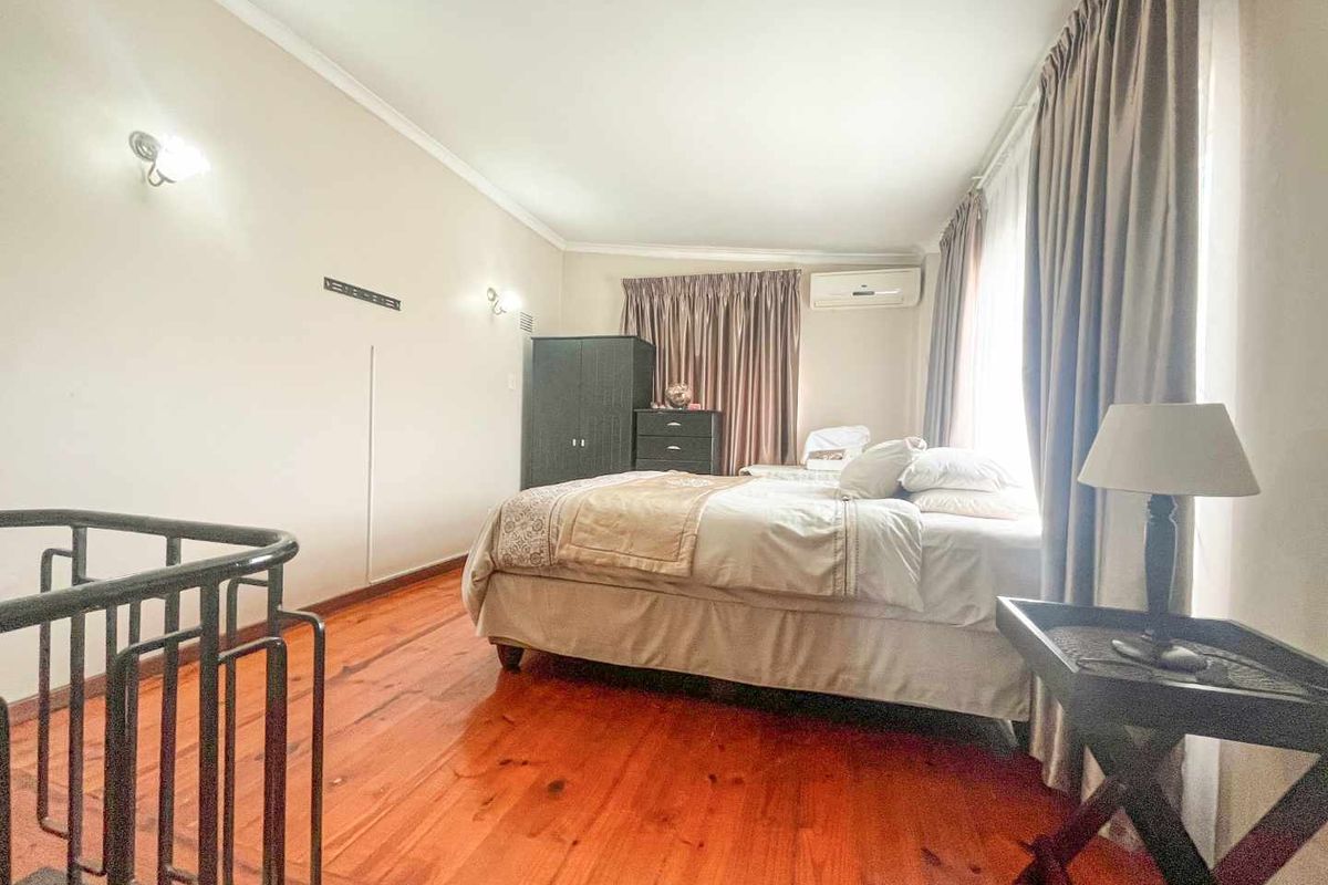 A bedroom featuring polished timber flooring, wall-mounted air conditioning unit, and large windows with curtain tracks.