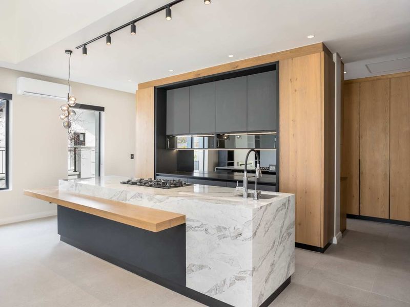 Modern kitchen featuring a large marble island with integrated gas cooktop, sleek dark cabinetry, wood-toned accents, and contemporary track lighting.