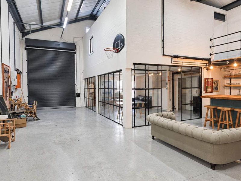 Spacious industrial open-plan area featuring polished concrete floors, exposed steel trusses, a built-in bar, and modern steel-framed glass partitions.