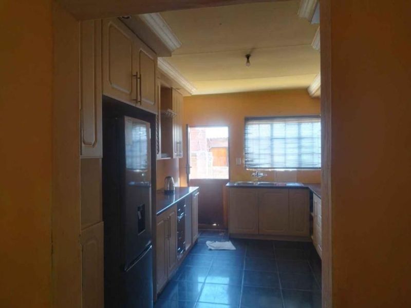 A functional kitchen featuring built-in cabinetry, laminate countertops, a stainless steel sink, and tiled flooring, with direct access to the exterior.