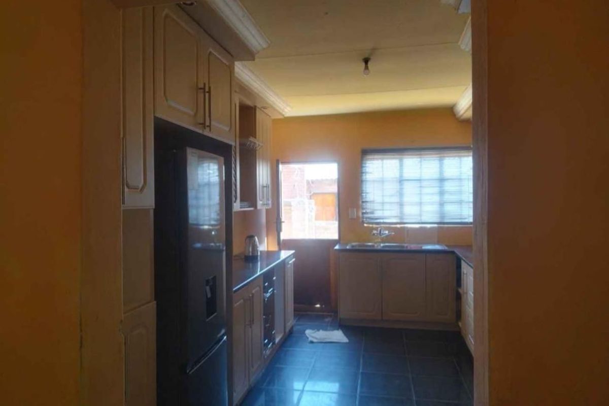 A functional kitchen featuring built-in cabinetry, laminate countertops, a stainless steel sink, and tiled flooring, with direct access to the exterior.