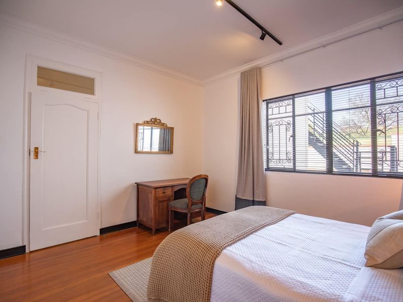 A well-maintained bedroom featuring polished hardwood flooring, track lighting, and a window fitted with security bars.