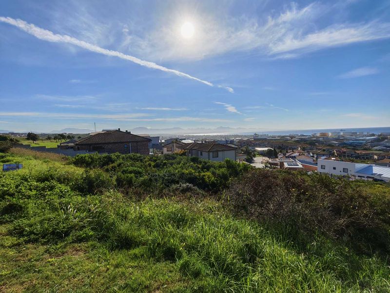 A scenic elevated view overlooking a residential neighborhood with distant mountain and coastal vistas under a clear blue sky.