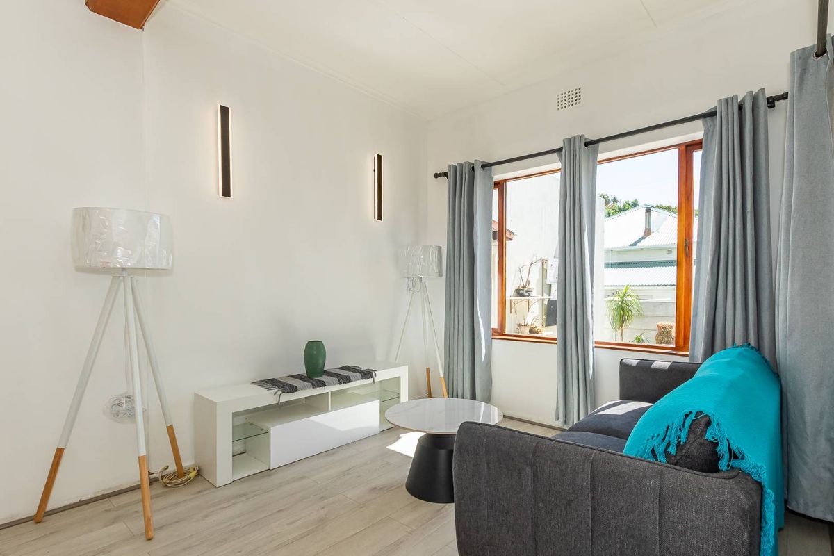 A bright living room featuring light wood-look flooring, modern wall-mounted lighting, and large windows that provide ample natural light.