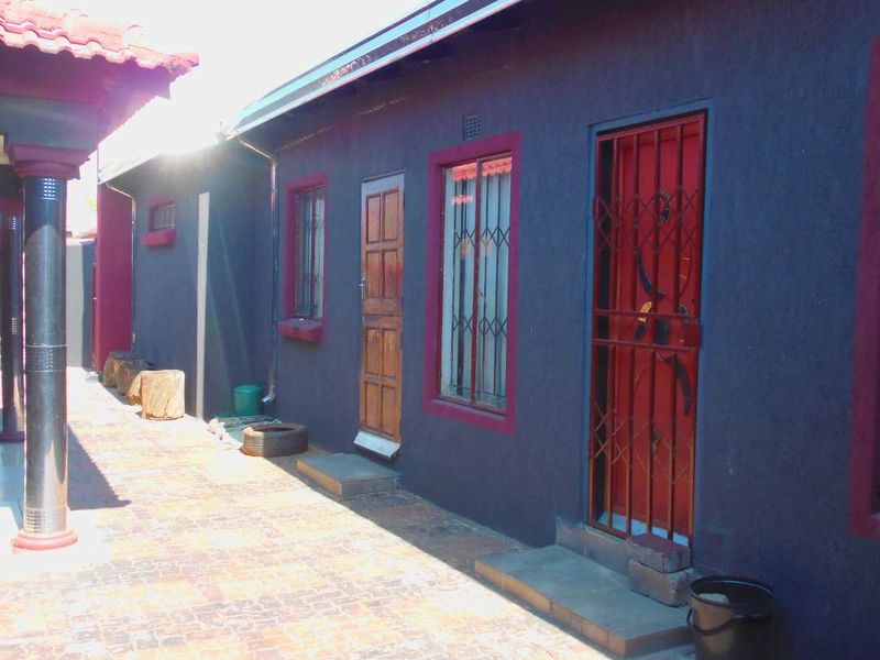 A side exterior view of the house featuring dark painted walls with red trim, brick paving, and security gates on the doors and windows.