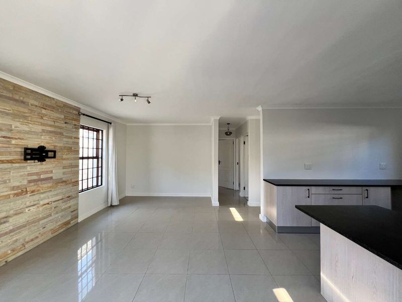 Spacious open-plan living and kitchen area featuring modern stone cladding, neutral floor tiles, and contemporary cabinetry, offering a bright and versatile living space.