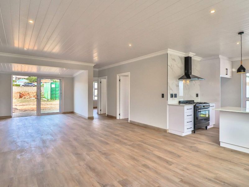 Spacious open-plan living area featuring modern laminate flooring, a contemporary kitchen with a gas stove, and sliding doors leading to the rear yard.