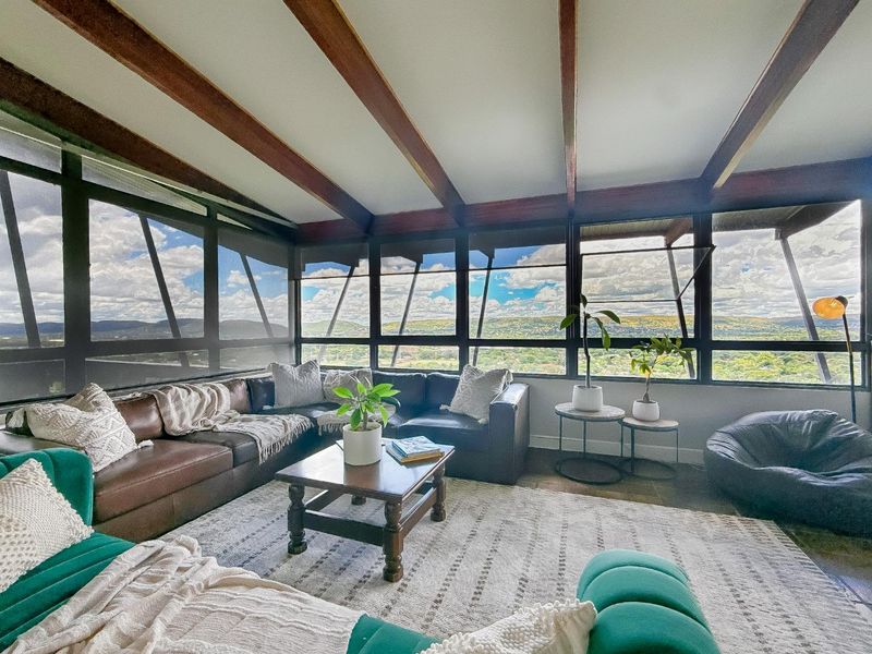A bright living room featuring exposed timber ceiling beams and expansive panoramic windows that offer extensive views of the surrounding landscape.