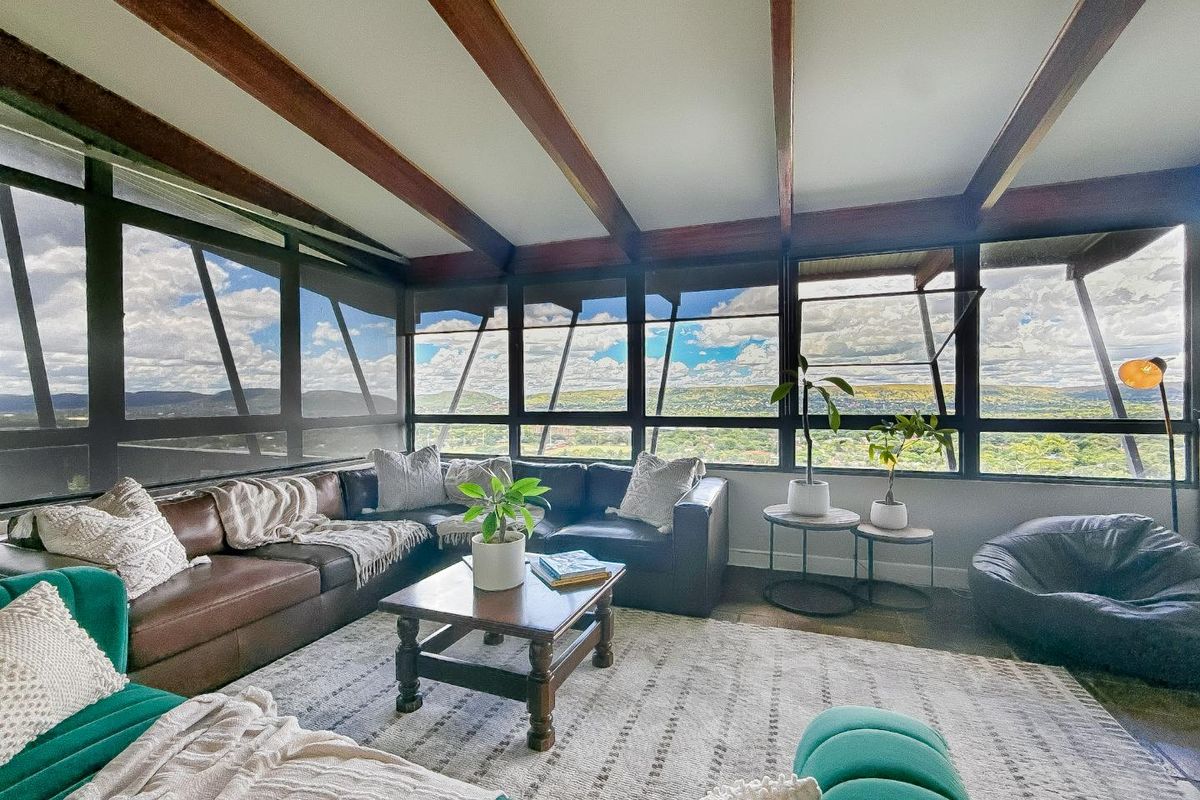 A bright living room featuring exposed timber ceiling beams and expansive panoramic windows that offer extensive views of the surrounding landscape.