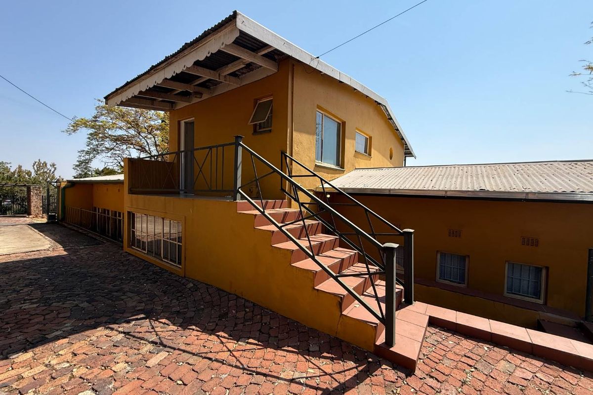 Rear exterior view of the townhouse featuring an external staircase, brick paved courtyard, and yellow painted facade with metal roofing.