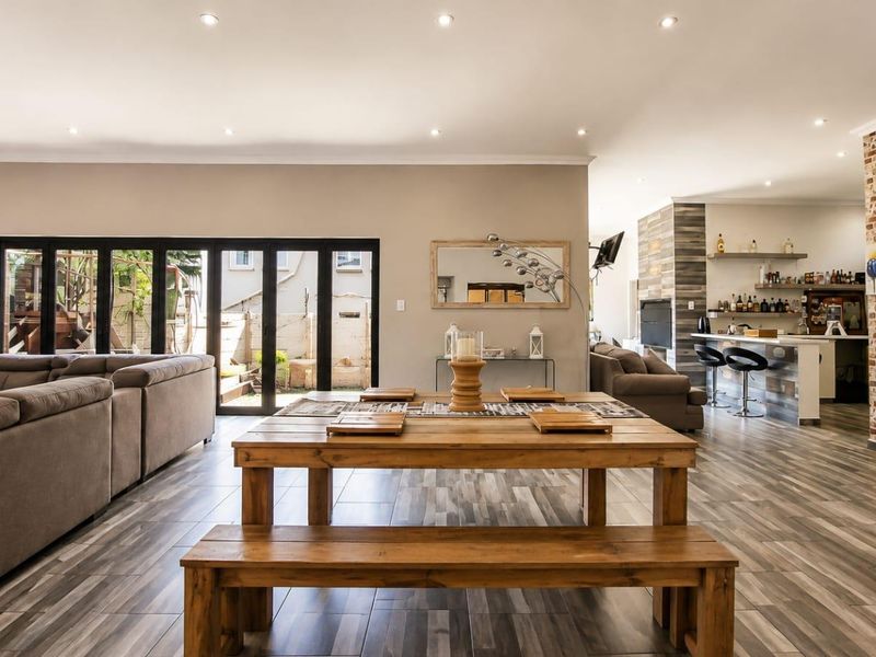 Spacious open-plan living and dining area featuring modern tiled floors, recessed lighting, an exposed brick feature wall, and seamless access to the outdoor patio.